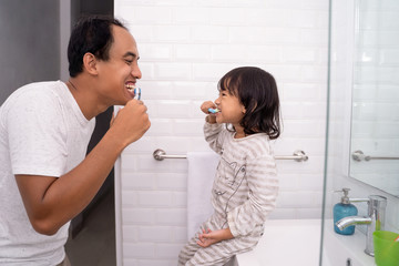 Girl brushing teeth with dad teaching child dental health tips