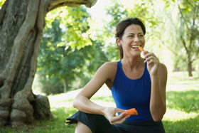 woman in the park smiling and eating carrots