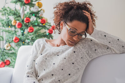 Woman looking stressed by a Christmas tree.
