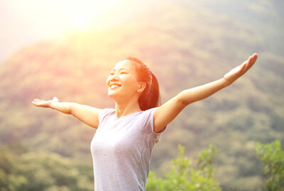 woman with arms out smiling on top of mountain with sunset
