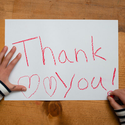 Kid writing Thank You with red crayon on white paper