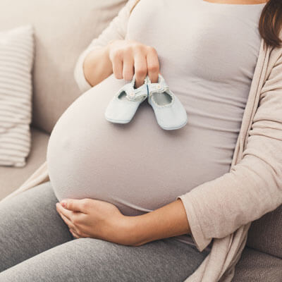 pregnant woman siting on couch holding baby shoes on belly